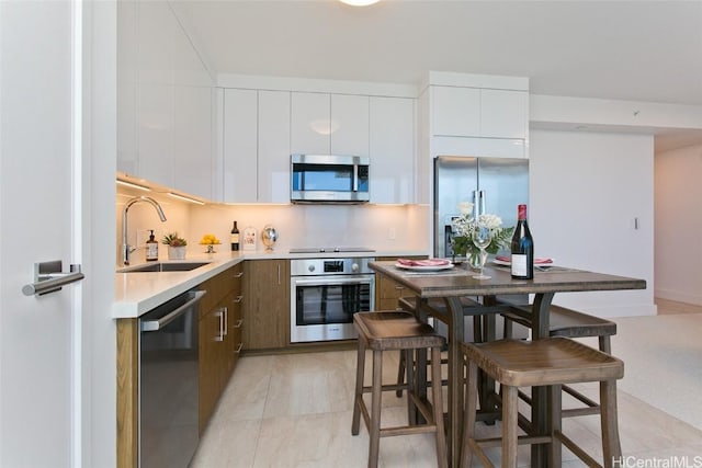 kitchen featuring white cabinets, sink, appliances with stainless steel finishes, and a breakfast bar area