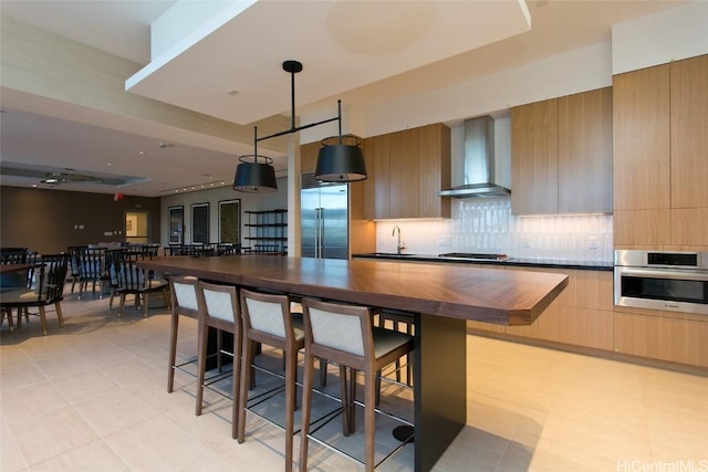 kitchen with sink, wall chimney exhaust hood, stainless steel appliances, tasteful backsplash, and light tile patterned floors