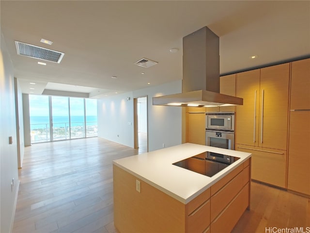 kitchen featuring a kitchen island, island exhaust hood, black electric stovetop, light wood-type flooring, and floor to ceiling windows