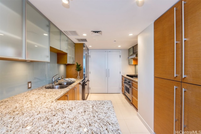 kitchen with exhaust hood, stainless steel appliances, sink, light tile patterned floors, and light stone counters