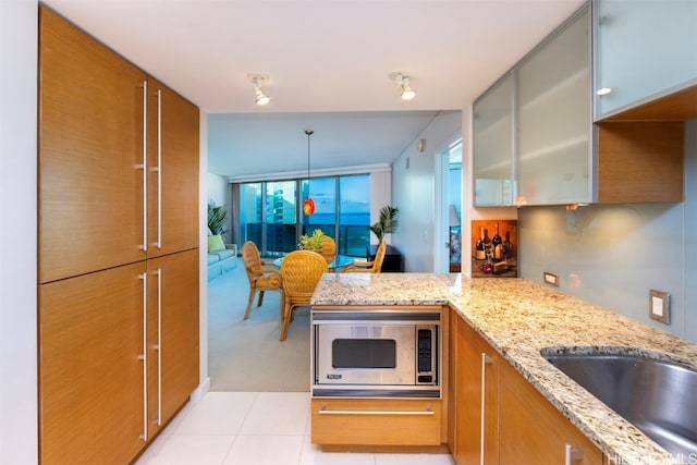 kitchen with kitchen peninsula, light stone counters, light tile patterned floors, stainless steel microwave, and decorative light fixtures