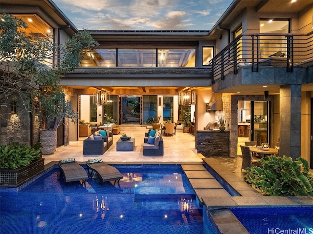 back house at dusk featuring a patio area, outdoor lounge area, and a balcony