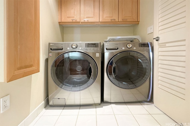 laundry room featuring washing machine and dryer, light tile patterned floors, and cabinets