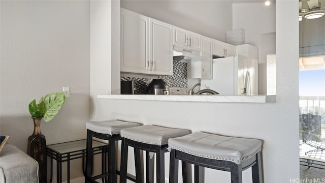 kitchen featuring white fridge with ice dispenser, kitchen peninsula, white cabinetry, and a breakfast bar area