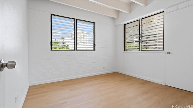 empty room featuring brick wall, beamed ceiling, and light wood-type flooring