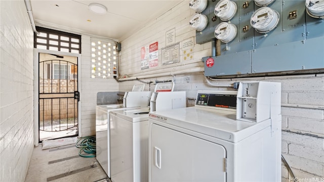 laundry room featuring brick wall and separate washer and dryer