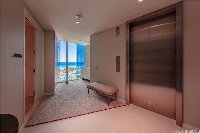 hall with a water view, a wall of windows, elevator, and light carpet