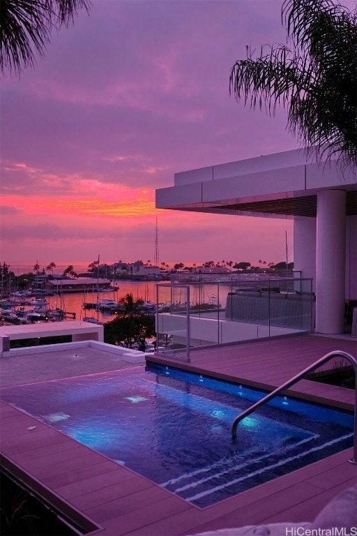 pool at dusk with a hot tub and a water view