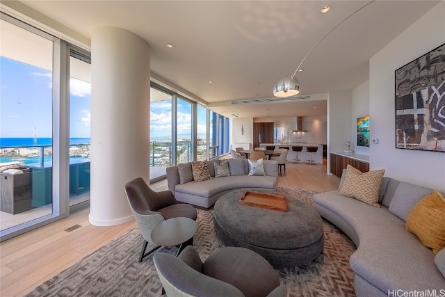 living room with floor to ceiling windows, light hardwood / wood-style flooring, and a water view