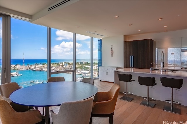 dining area featuring sink, a wall of windows, a water view, and light hardwood / wood-style floors