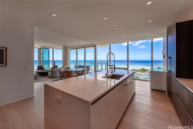 kitchen with white cabinetry, a kitchen island with sink, light wood-type flooring, sink, and a water view