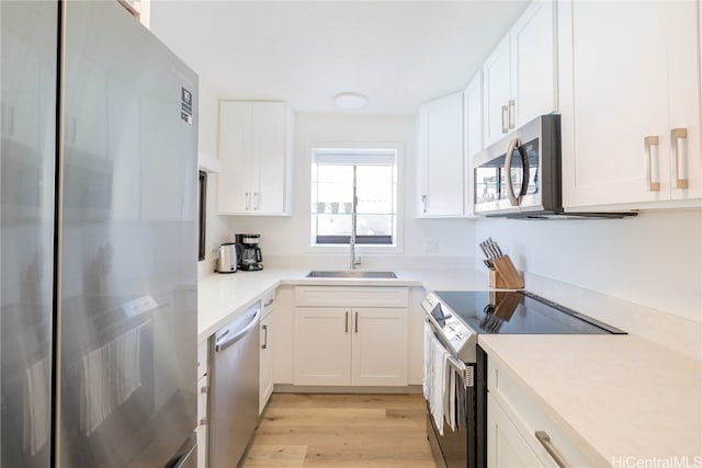 kitchen with appliances with stainless steel finishes, white cabinetry, sink, and light hardwood / wood-style floors