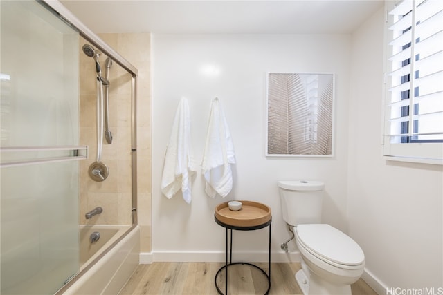 bathroom with toilet, wood-type flooring, and bath / shower combo with glass door