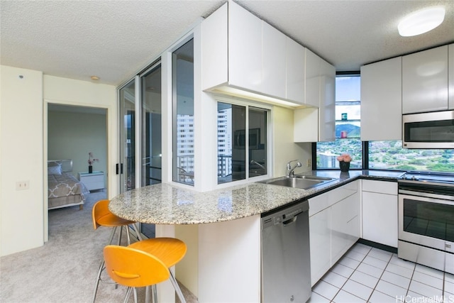 kitchen with white cabinets, appliances with stainless steel finishes, a textured ceiling, light colored carpet, and sink