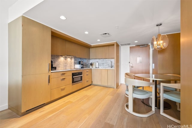 kitchen featuring decorative backsplash, stainless steel oven, an inviting chandelier, light brown cabinetry, and light hardwood / wood-style floors