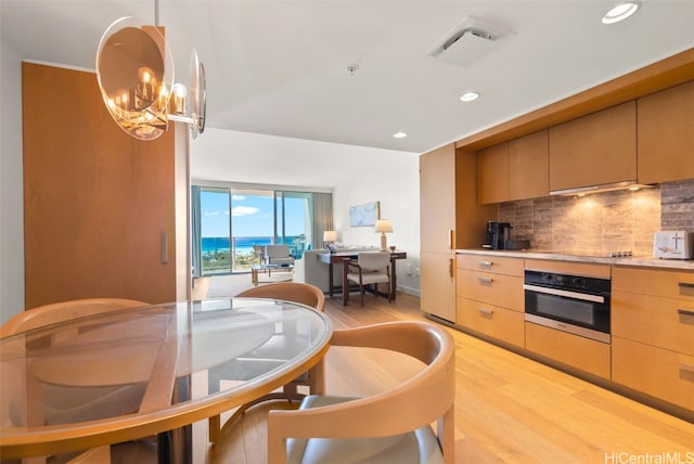 kitchen featuring tasteful backsplash, light brown cabinetry, stainless steel oven, light hardwood / wood-style floors, and a chandelier