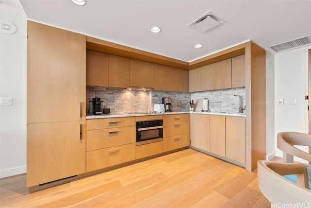 kitchen with decorative backsplash, oven, sink, light wood-type flooring, and light brown cabinetry