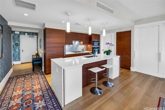 kitchen with a center island with sink, a kitchen breakfast bar, pendant lighting, stainless steel gas stovetop, and light hardwood / wood-style floors