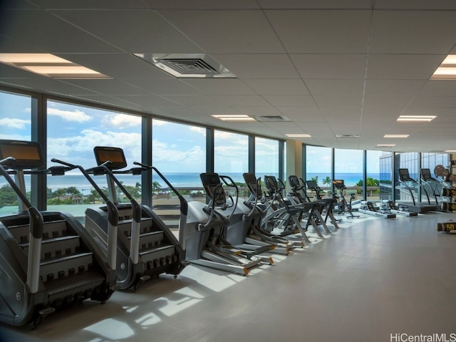 gym with a water view, a paneled ceiling, and a wall of windows