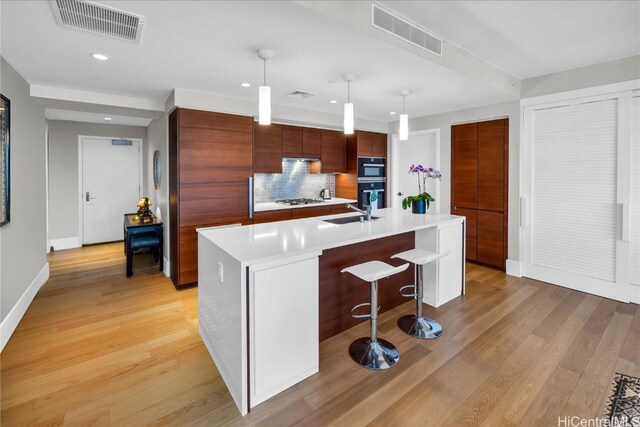 kitchen featuring a kitchen breakfast bar, an island with sink, pendant lighting, and light wood-type flooring