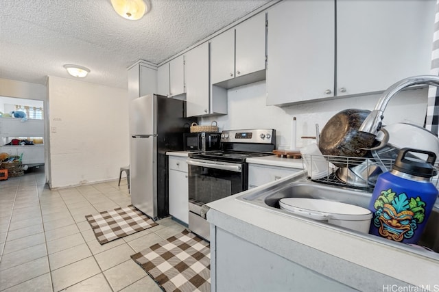 kitchen featuring appliances with stainless steel finishes, white cabinetry, light tile patterned flooring, and a textured ceiling