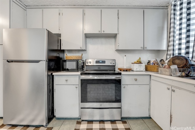 kitchen featuring appliances with stainless steel finishes, a textured ceiling, white cabinets, and light tile patterned flooring