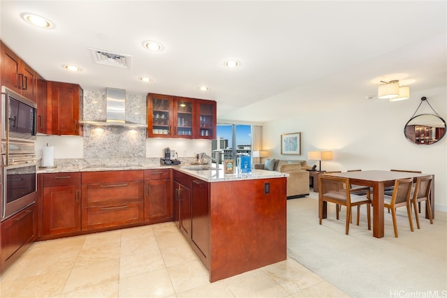 kitchen with wall chimney range hood, oven, built in microwave, light stone counters, and tasteful backsplash