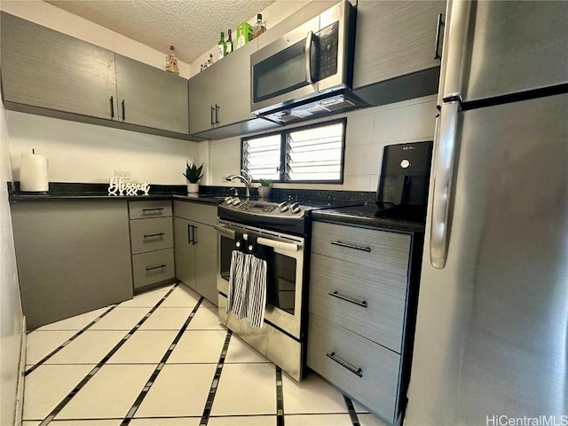 kitchen with dark countertops, gray cabinets, appliances with stainless steel finishes, a textured ceiling, and a sink