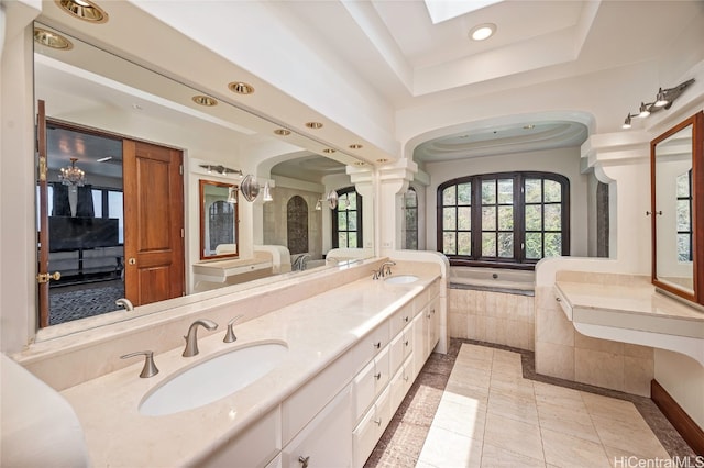 bathroom featuring a tray ceiling, ornate columns, tiled tub, vanity, and tile patterned flooring