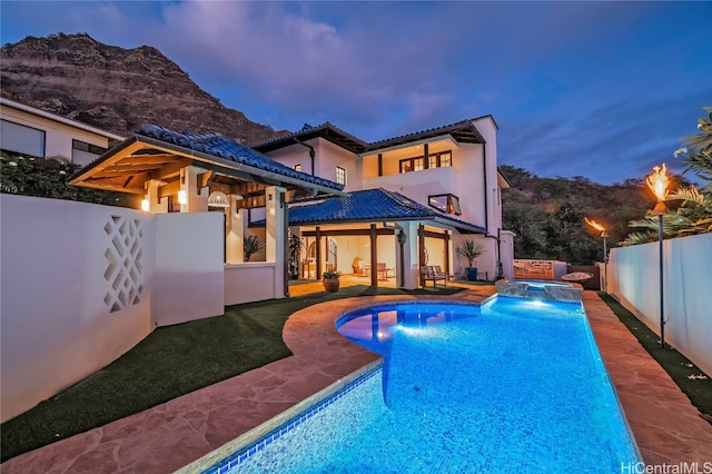 pool at dusk with a mountain view, pool water feature, and a patio area