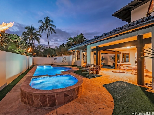 pool at dusk with an in ground hot tub and a patio area