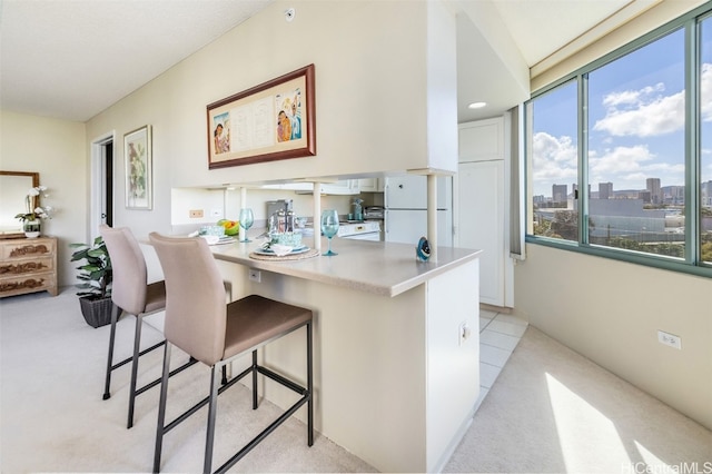 kitchen with light colored carpet, a breakfast bar, kitchen peninsula, and white refrigerator