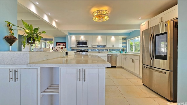 84-879 Moua St, Waianae, HI 96792 - kitchen featuring white cabinetry, light tile patterned floors, appliances with stainless steel finishes, kitchen peninsula, and light stone countertops
