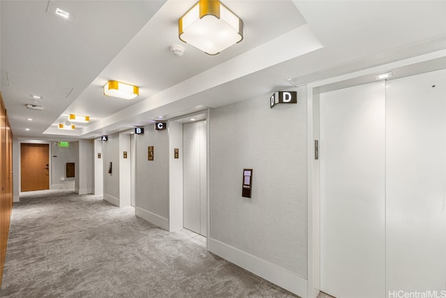 hallway with elevator, carpet, and a tray ceiling