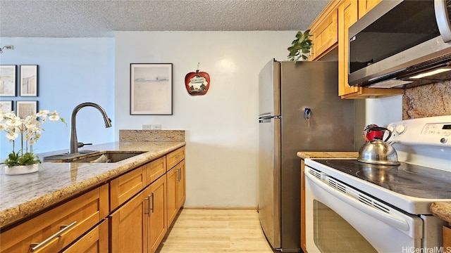 kitchen with a textured ceiling, light stone countertops, light hardwood / wood-style flooring, white electric stove, and sink