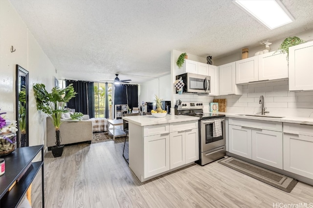 kitchen featuring kitchen peninsula, stainless steel appliances, sink, light wood-type flooring, and white cabinetry