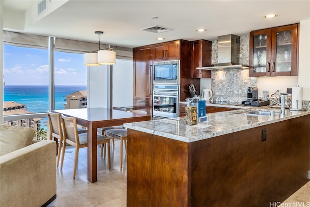 kitchen with wall chimney range hood, stainless steel appliances, pendant lighting, a water view, and light stone counters