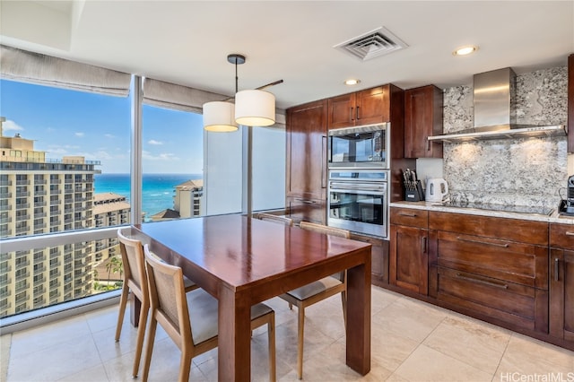 kitchen with wall chimney range hood, black appliances, backsplash, decorative light fixtures, and a water view