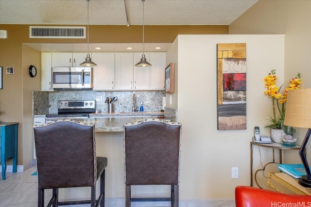 kitchen featuring hanging light fixtures, stainless steel appliances, white cabinets, light stone counters, and decorative backsplash