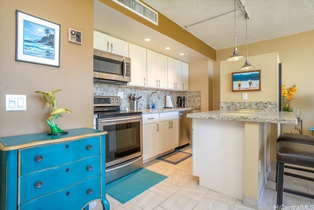 kitchen with white cabinets, backsplash, a textured ceiling, pendant lighting, and stainless steel appliances