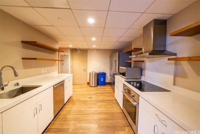 kitchen with wall chimney range hood, white cabinetry, stainless steel appliances, and sink