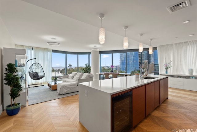 kitchen featuring light parquet flooring, sink, an island with sink, hanging light fixtures, and wine cooler