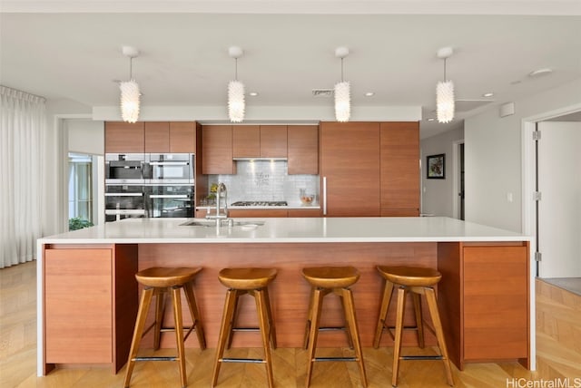 kitchen with modern cabinets, a spacious island, tasteful backsplash, brown cabinetry, and light countertops