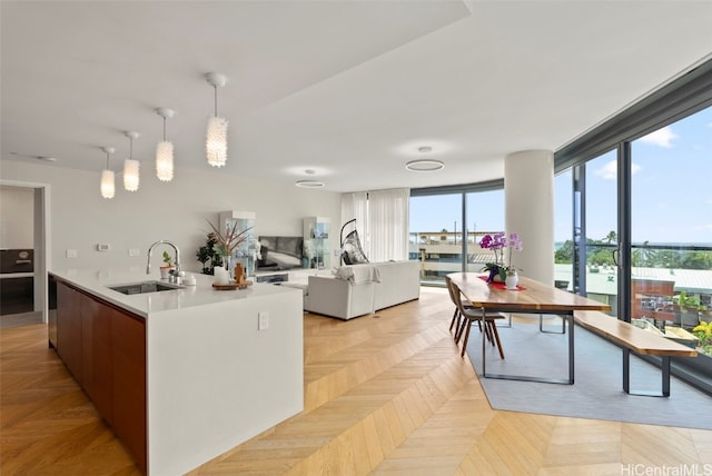 kitchen with a sink, open floor plan, pendant lighting, light countertops, and a kitchen island with sink