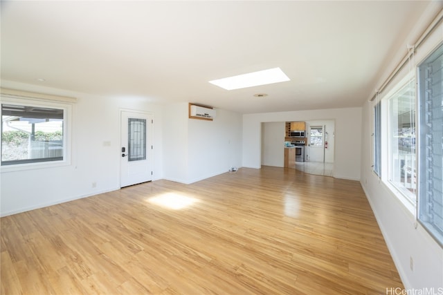 unfurnished living room with light hardwood / wood-style flooring, an AC wall unit, and a skylight