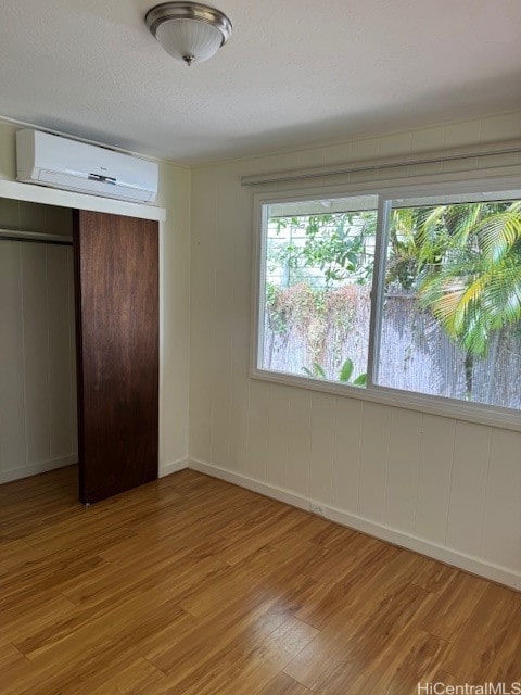 unfurnished bedroom featuring a closet, an AC wall unit, and light wood-type flooring