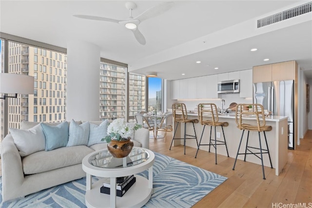 living room featuring sink, light hardwood / wood-style floors, a wall of windows, and ceiling fan