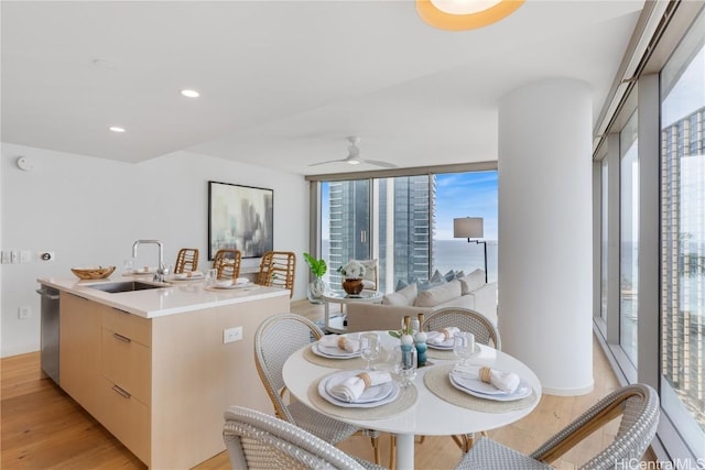 kitchen featuring a kitchen island with sink, sink, stainless steel dishwasher, ceiling fan, and light wood-type flooring