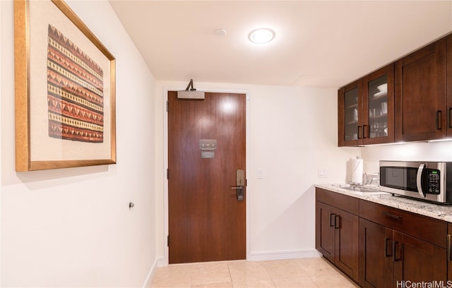 kitchen with dark brown cabinetry, light stone counters, and light tile patterned floors