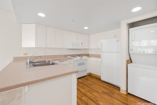 kitchen with kitchen peninsula, white appliances, stacked washer and dryer, and white cabinetry